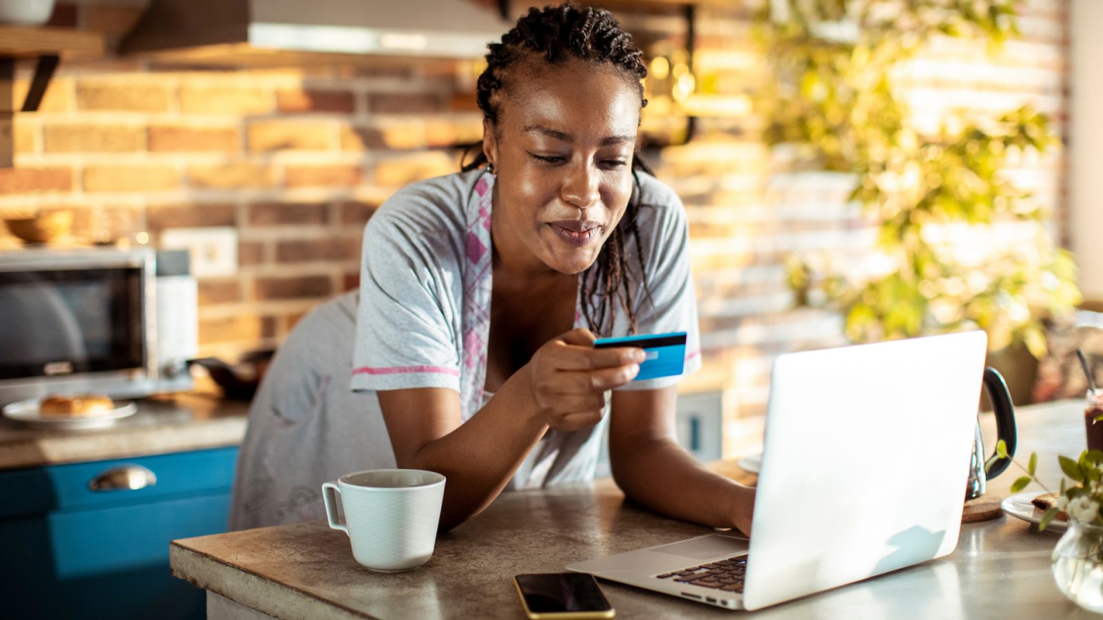 A woman standing near a laptop smiles as she looks at a credit card.