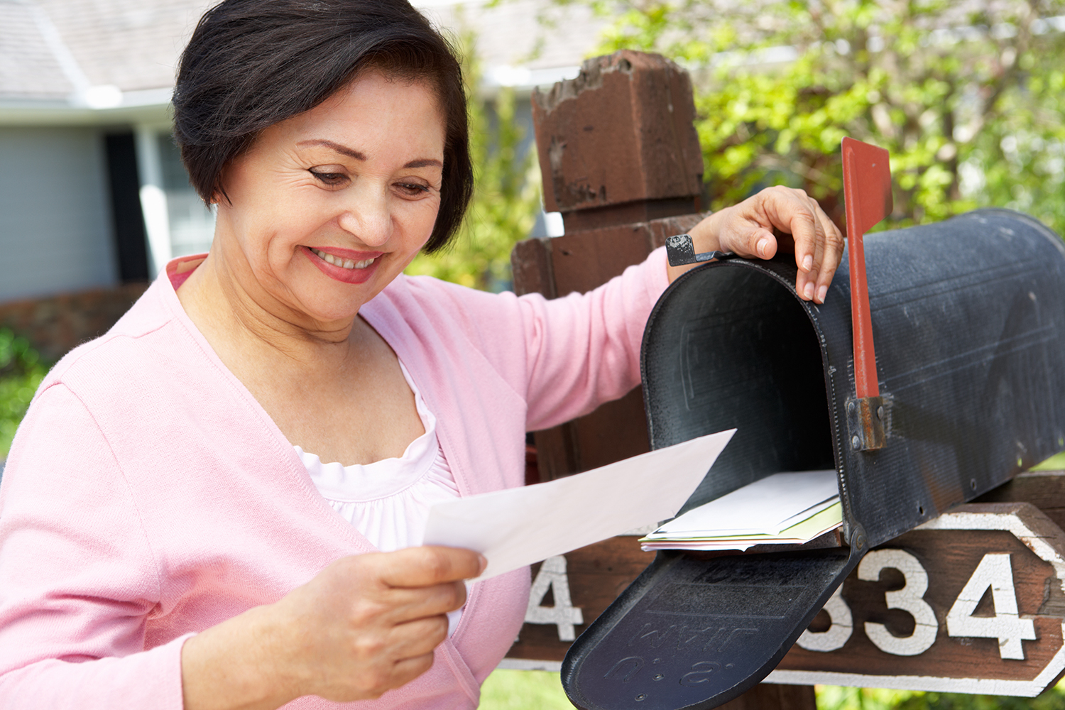 An adult woman smiles as she looks at mail while standing at her mailbox. Individuals from all generations appreciate the value, convenience and personal touch of direct mail.